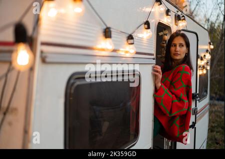 Une femme caucasienne en pull tricoté rouge surdimensionné voyage à motorhome en automne. Banque D'Images