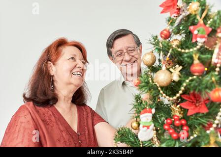 Joyeux couple hispanique senior souriant tout en décorant leur arbre de Noël traditionnel à la maison. Le plaisir de passer les vacances ensemble. Banque D'Images