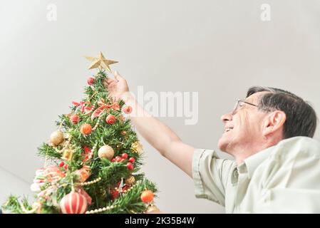 Joyeux latiman senior souriant alors qu'il met une étoile d'or sur le dessus de son arbre de Noël, la joie de passer les vacances à la maison. Banque D'Images