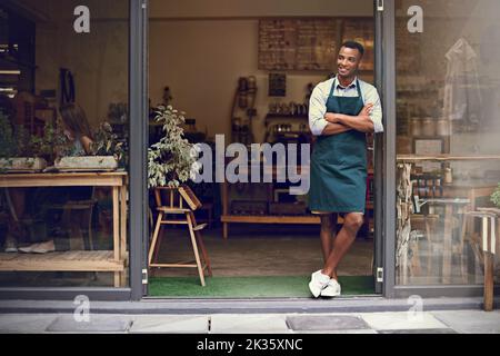 HES a eu de grands rêves pour sa petite entreprise. Un jeune barista ambitieux se tenant à l'entrée d'un café. Banque D'Images