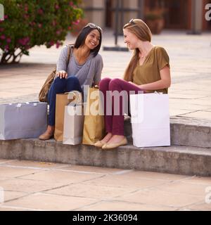 Faites vos courses jusqu'à épuisement. Deux jeunes femmes discutant sur les marches après une longue et réussie journée de shopping. Banque D'Images