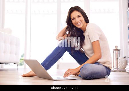 Les avantages du travail à domicile. Une jeune femme assise sur le sol avec son ordinateur portable. Banque D'Images