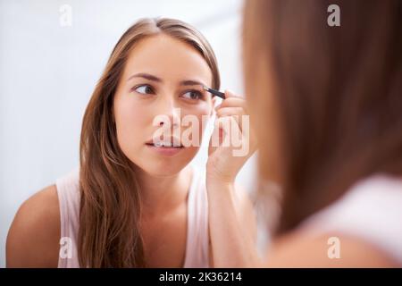 Créer la voûte plantaire parfaite. Une jeune femme en train de touiller ses sourcils devant un miroir. Banque D'Images