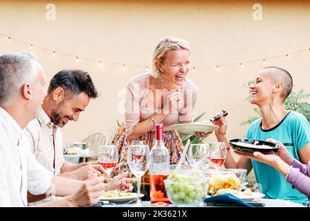 Des personnes matures célébrant une fête barbecue partageant sa nourriture avec ses amis. Jolie femme apporte une salade à la table. Concept de style de vie. Banque D'Images