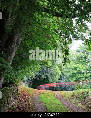 Au sommet de la Cisjordanie, à Winster, les feux de stop d’une voiture laissent une belle courbe de lumière rouge un jour terne, car elle disparaît sur la rive. Banque D'Images