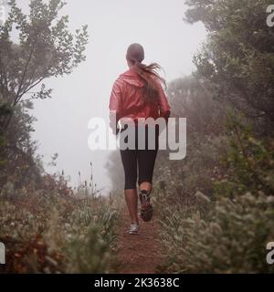 Elle a trouvé le chemin de la longévité. Vue arrière d'une femme qui court sur un sentier un matin brumeux. Banque D'Images