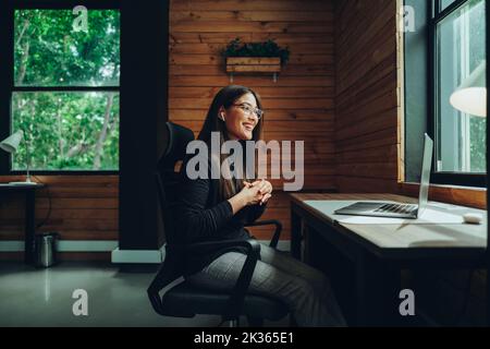 Jeune femme d'affaires joyeuse ayant un appel vidéo dans un espace de travail commun moderne. Une femme entrepreneure heureuse qui communique avec ses partenaires commerciaux, wh Banque D'Images