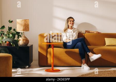 Bonne femme d'affaires souriant à la caméra tout en étant assise sur un canapé dans un hall de bureau. Jeune femme d'affaires gaie travaillant dans un collègue créatif de Banque D'Images