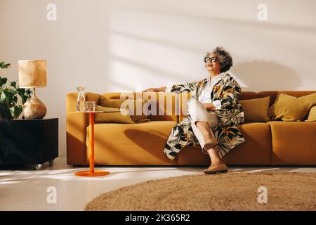 Femme d'affaires mûre souriant en s'asseyant sur un canapé dans le hall d'un bureau. Femme d'affaires gaie travaillant dans un bureau de collègue créatif. Banque D'Images