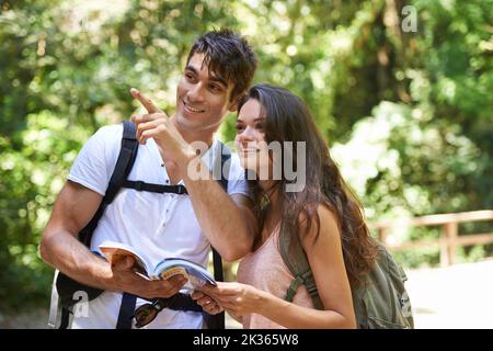 Allons dans cette direction... un jeune couple debout avec un guide tout en randonnée dans une forêt. Banque D'Images