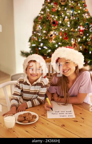 Lettres au Père Noël. Frère et sœur écrivant une lettre au Père Noël et lui laissant du lait et des biscuits. Banque D'Images