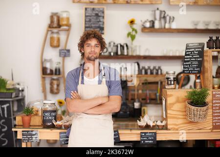 Toujours un visage sympa au café. Portrait d'un barista masculin se tenant au comptoir d'un café. Banque D'Images
