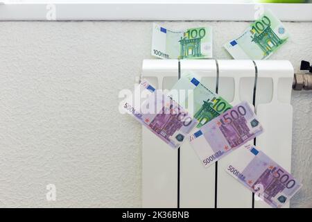 Billets en papier de 100 et 500 euros sur un petit radiateur blanc pour le chauffage de la maison. Banque D'Images