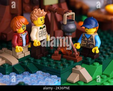 Tambov, Fédération de Russie - 22 juin 2022 trois mini-figurines Lego - homme et deux enfants, cuisine de nourriture sur un feu de camp. Gros plan Banque D'Images