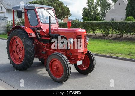 Tracteur rouge vintage, soigneusement restauré oldtimer, conduite sur la route à travers le village, mouvement plus bleu, sélection de focus Banque D'Images