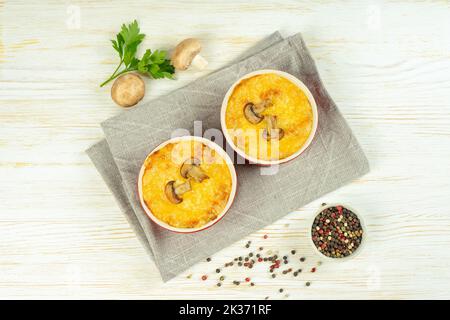 Cocotte de poulet et de champignons à la croûte dorée, julienne au fromage au four, gratin crémeux en portion de ramequin sur fond de bois blanc. FR Banque D'Images