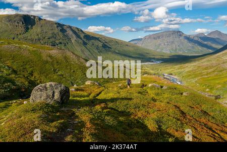 Randonnée femelle avec sac à dos lourd et équipement de marche dans la vallée de montagne dans l'Arctique lointain le jour ensoleillé d'été.vallée de Noajdevagge avec montagne Laddebakte Banque D'Images