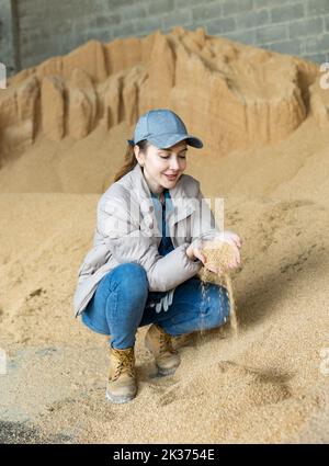 Femme agriculteur détenant une poignée de cosse de soja, dans le stockage de nourriture pour animaux Banque D'Images