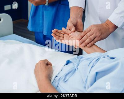 La main du médecin en blouse de laboratoire blanche tient la main du patient âgé allongé sur le lit pour vérification afin d'examiner le pouls cardiaque par les doigts dans la salle de récupération Banque D'Images