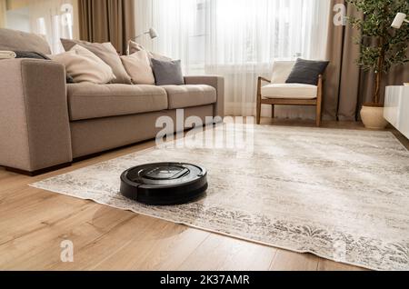 Aspirateur robot travaillant sur la moquette dans le nouveau salon dans les couleurs beige clair et gris Banque D'Images