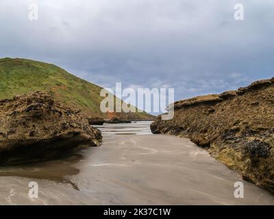 Chemin de sable jusqu'au bord de l'eau entre les affleurements rocheux et la crête de colline menant à un ciel spectaculaire couvert. Banque D'Images