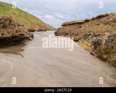 Chemin de sable jusqu'au bord de l'eau entre les affleurements rocheux et la crête de colline menant à un ciel spectaculaire couvert. Banque D'Images