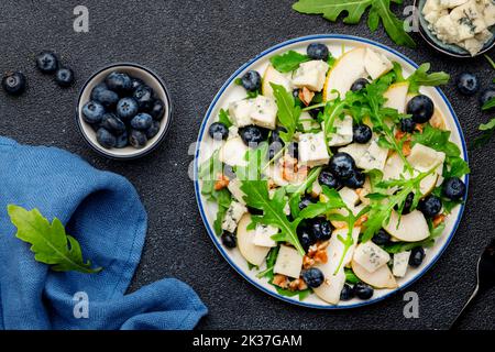 Delicious arugula salad with pears, blueberries, roquefort cheese and walnuts. Black kitchen table background, top view Banque D'Images