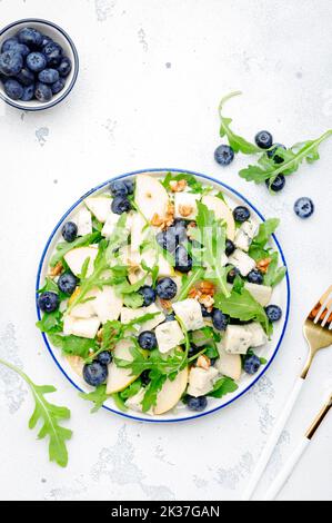 Delicious arugula salad with pears, blueberries, roquefort cheese and walnuts. Black kitchen table background, top view Banque D'Images