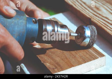 L'homme les mains avec brosse rotative électrique disque métal ponçage d'un morceau de bois. Le travail du bois à l'extérieur. Banque D'Images