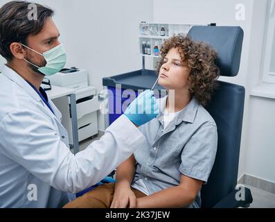 médecin prenant un écouvillon nasopharyngé de garçon frisé pour examen dans un laboratoire médical pour détecter les bactéries du nez ou le coronavirus. Test PCR Banque D'Images