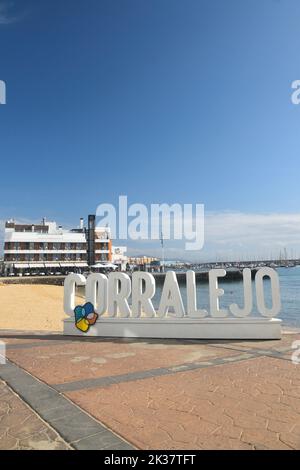 Panneau Corralejo en pierre blanche avec plage et hôtels en arrière-plan. Journée ensoleillée avec ciel bleu. Banque D'Images