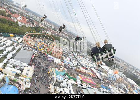 25 septembre 2022, Bavière, Munich : depuis un carrousel à chaînes géantes, la grande roue et les montagnes russes à cinq boucles sont visibles sous un ciel couvert et sous une légère pluie. La Wiesn aura lieu de 17 septembre à 3 octobre 2022. Photo: Felix Hörhager/dpa Banque D'Images