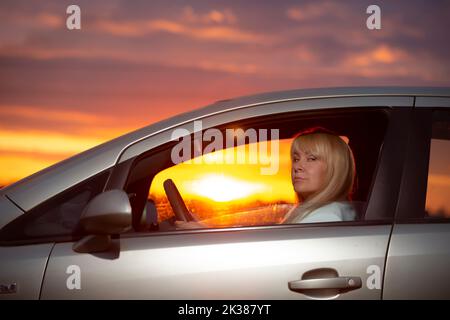 Femme d'âge moyen conduisant une voiture contre le coucher de soleil ciel.étranger Banque D'Images