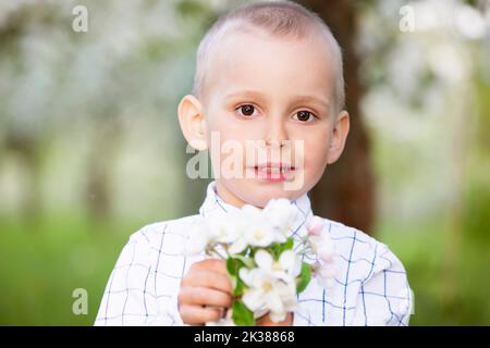 Un enfant heureux dans un jardin de printemps en pleine floraison se réjouit, sourit. Banque D'Images