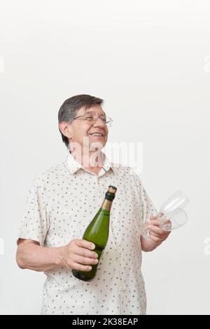 Homme hispanique senior souriant en tenant une bouteille de champagne ou de cidre et une paire de verres. Concept de toast festif. Banque D'Images