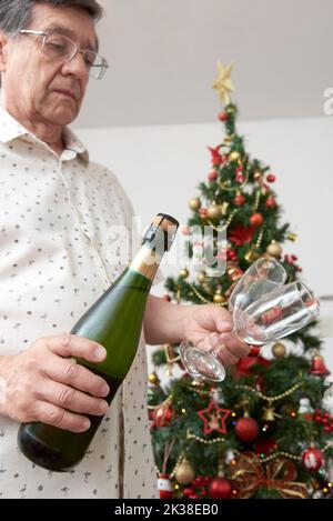 Homme méconnaissable tenant une bouteille de champagne ou de cidre et une paire de verres avec un sapin de Noël en arrière-plan. Concept de toast festif. Banque D'Images