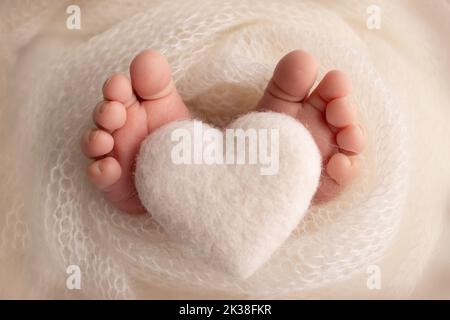 Coeur blanc tricoté dans les jambes d'un bébé. Pieds doux d'un nouveau né dans un blanc. Banque D'Images