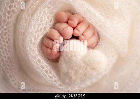 Coeur blanc tricoté dans les jambes d'un bébé. Pieds doux d'un nouveau né dans une couverture. Banque D'Images