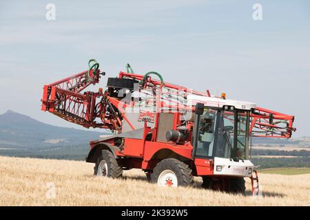 Un pulvérisateur automoteur Bateman 4000 dans un champ d'orge repliant sa rampe de pulvérisation, avec Bennachie, Aberdeenshire, en arrière-plan Banque D'Images