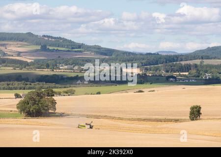Une vue panoramique sur les terres arables en direction de Tillifourie et de la Suie dans l'Aberdeenshire, avec une moissonneuse-batteuse opérant dans un champ de céréales Banque D'Images