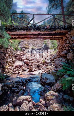 Un pont en bois au-dessus d'un ruisseau de montagne contre un ciel anxieux. Banque D'Images