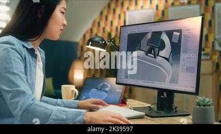 Femme asiatique indépendante travaillant à domicile et créant 3D prototypes de micro-casque VR moderne dans un logiciel professionnel de modélisation 3D utilisant un pc et une tablette numérique Banque D'Images