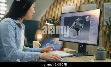 Femme asiatique indépendante travaillant à domicile et créant 3D prototypes de micro-casque VR moderne dans un logiciel professionnel de modélisation 3D utilisant un pc et une tablette numérique Banque D'Images