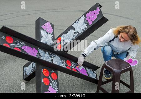 Dnipro, Ukraine - 10 septembre 2022: Femme artiste peinture métal anti-char obstacle tchèque hérisson dans la ville de première ligne pendant la guerre russo-ukrainienne o Banque D'Images