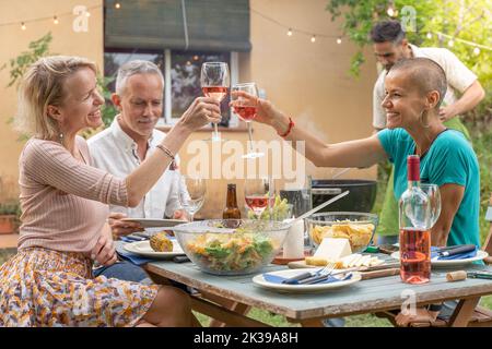 Des amis de groupe qui se coutent avec un grand sourire autour de la table dans le patio de la maison. Banque D'Images