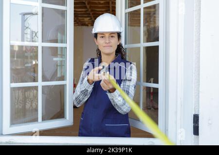 femme de travail souriante dans une salopette à l'aide d'un mètre ruban Banque D'Images