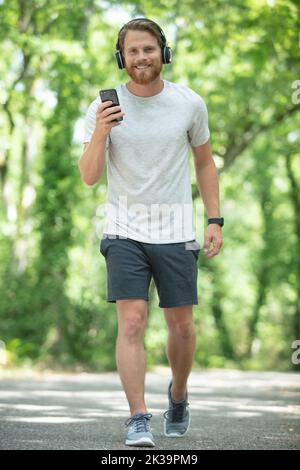 homme barbu avec un casque souriant et courant dans le parc Banque D'Images