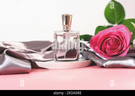 bouteille de parfum avec rose rose et soie grise satin tissu feuille sur fond rose. parfum floral, femme luxe beauté cosmétique Banque D'Images