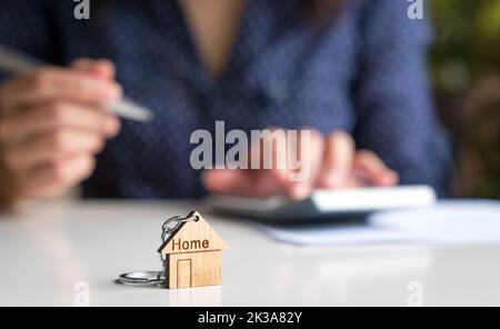 Porte-clés à la maison avec femme sur la calculatrice à l'arrière-plan. Concept d'évaluation ou d'investissement immobilier. Banque D'Images