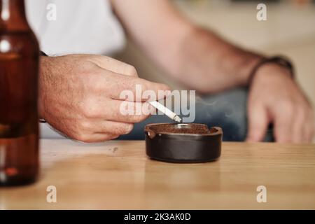 Mains d'un homme mûr secouant les cendres dans le cendrier de la table Banque D'Images